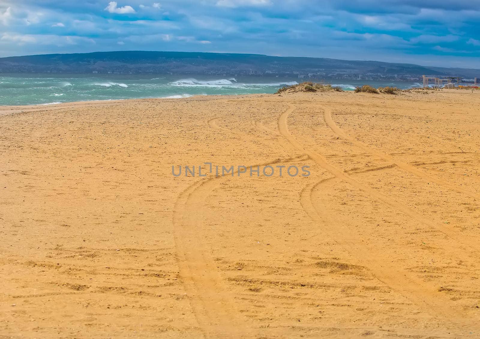 Traces of automobile wheels on seashore. Mountainous background.