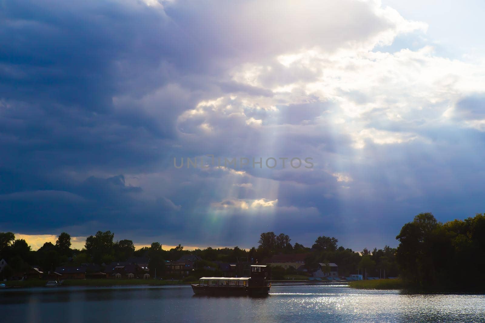 Rays of the sun making their way through the clouds over the lake, with houses on the shore.