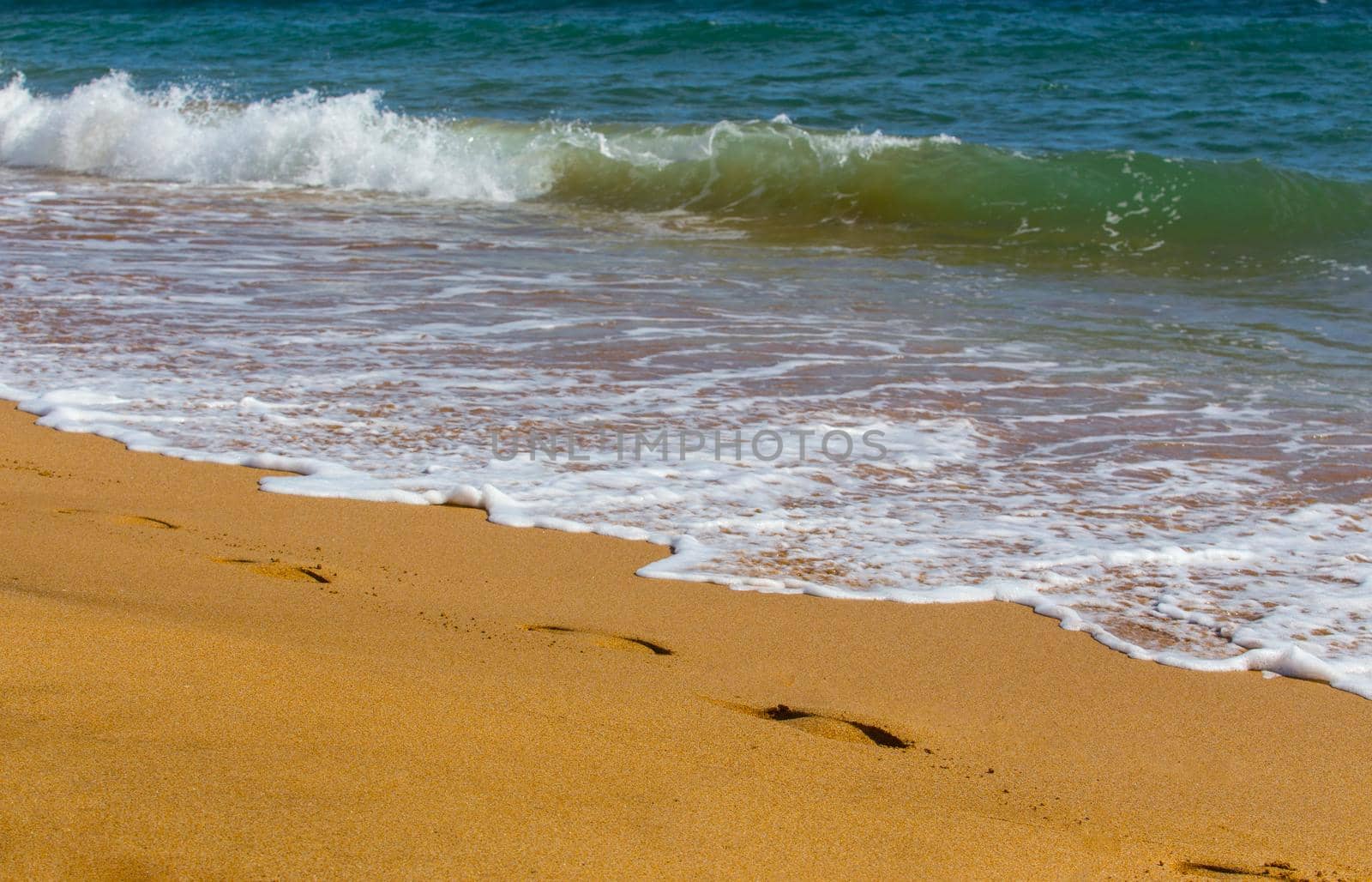 Sea waves roll on to shore. Sea foam. Traces of human feet. Closeup.