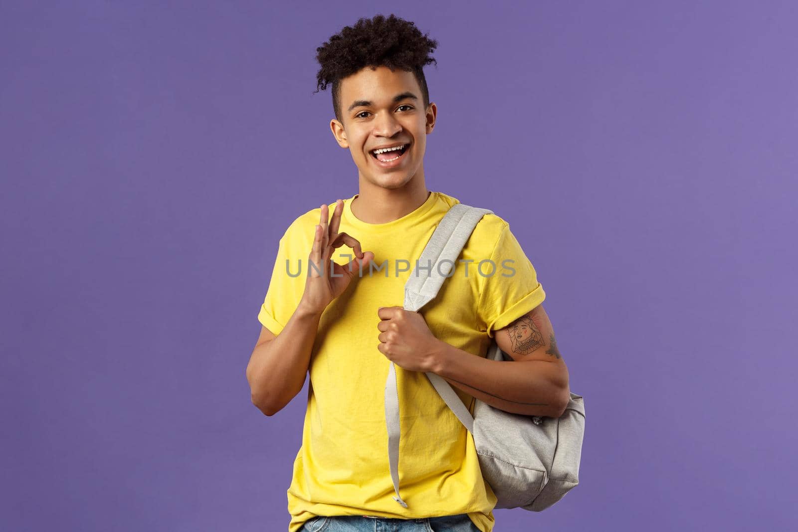 Back to school, university concept. Portrait of young handsome hipster guy, student with backpack assure test be good, show okay sign, chill and relax no worried, all ok, purple background.
