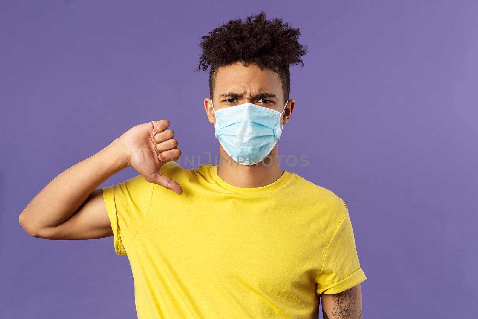 Medicine, covid19, coronavirus and people concept. Close-up portrait of displeased young man disapprove person ignores social distancing protocol, show thumbs-up, think its bad, purple background.
