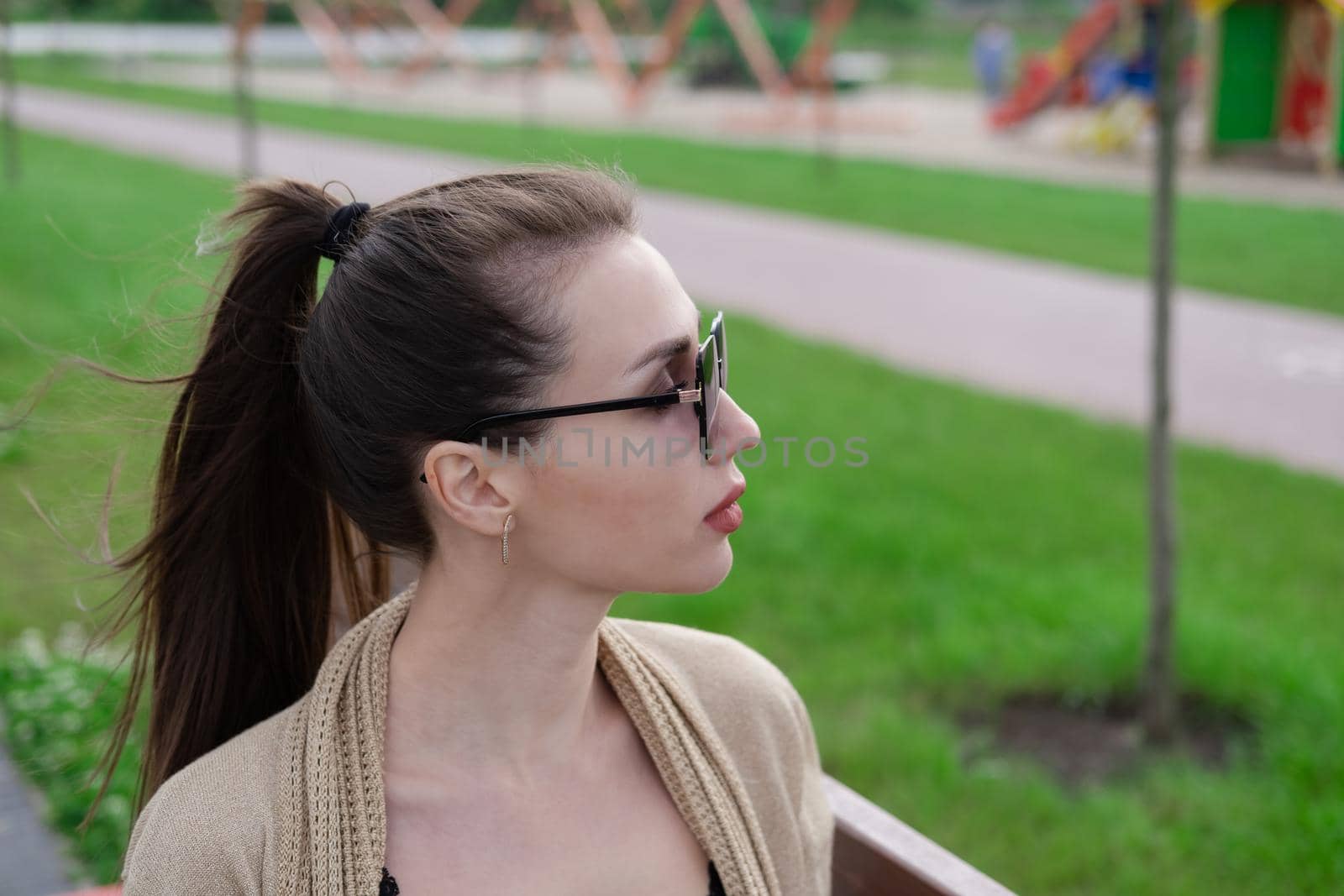 attractive brunette woman sitting on a bench in park. fashion clothes, stylish look by oliavesna