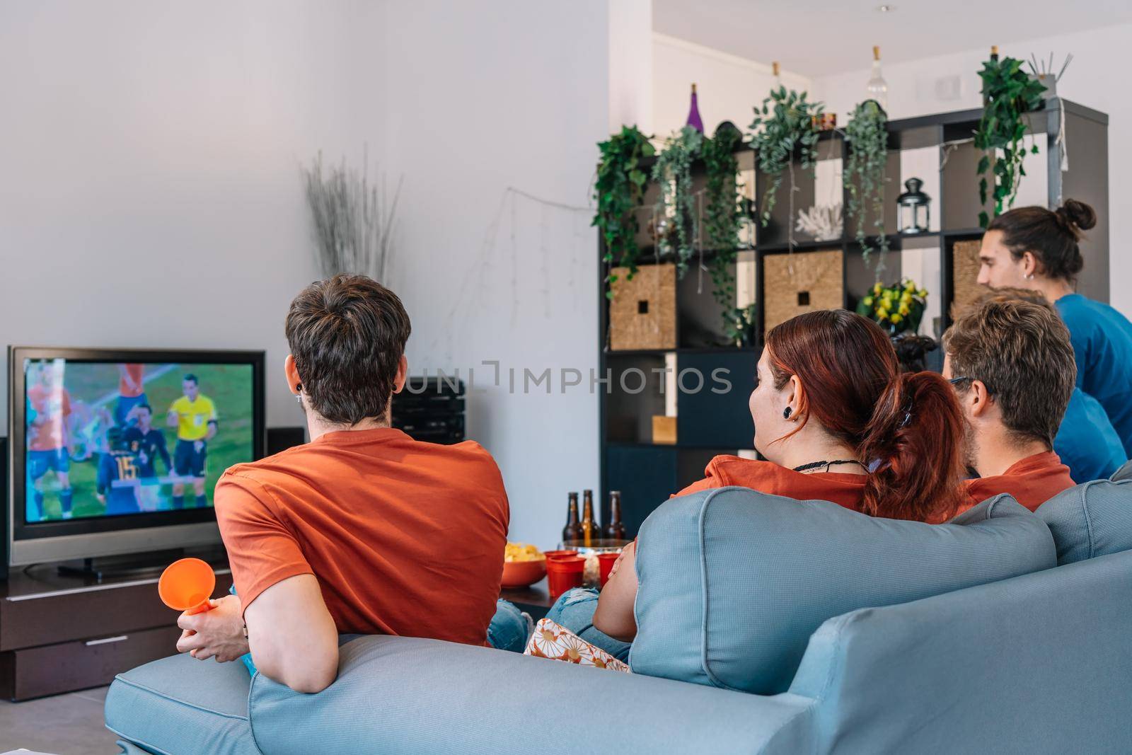 group of friends relaxing on the sofa at home watching a soccer match, broadcast on television. by CatPhotography