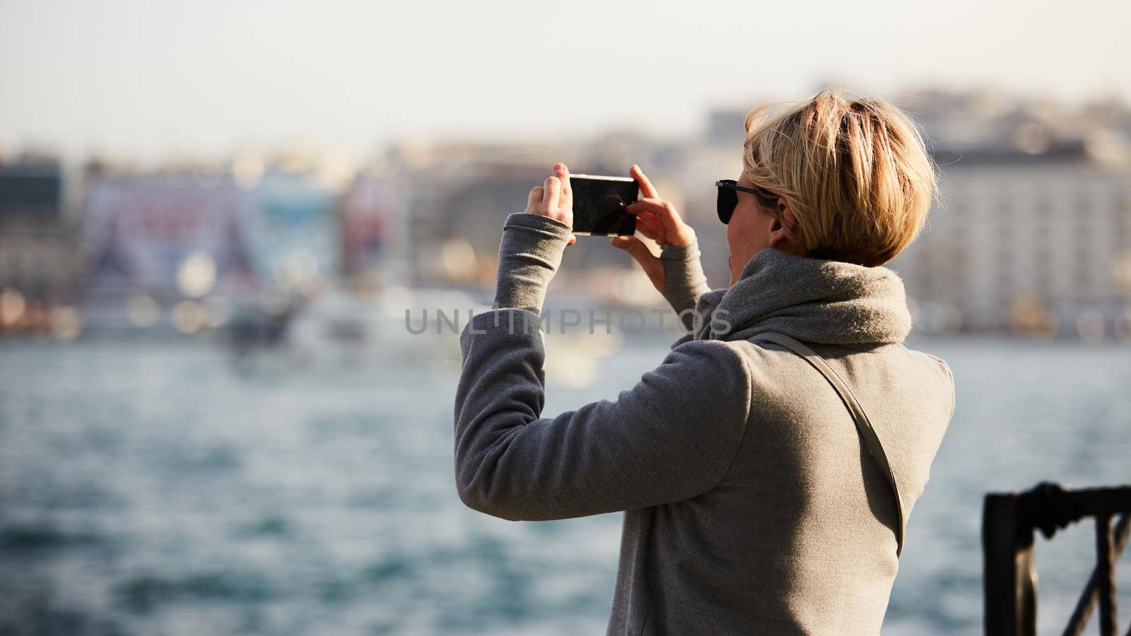 Rear back view young woman hold cellphone take photo enjoy cityscape view, from smartphone camera. Tourist capture moment, photographing famous landmarks scenery. Travel destinations concept