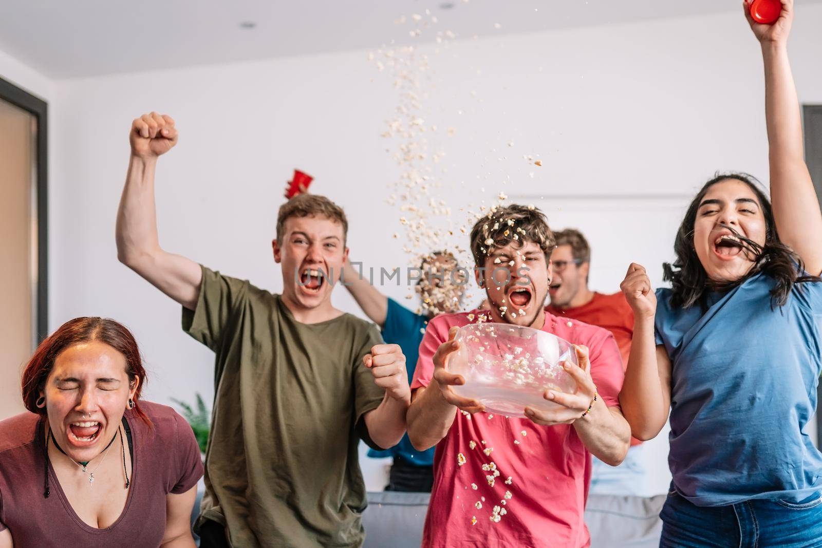 excited young people throwing popcorn in the air after their team's victory, broadcast on television. group of young people watching football at home. leisure concept. happy and cheerful. natural light in the living room at home. trumpet
