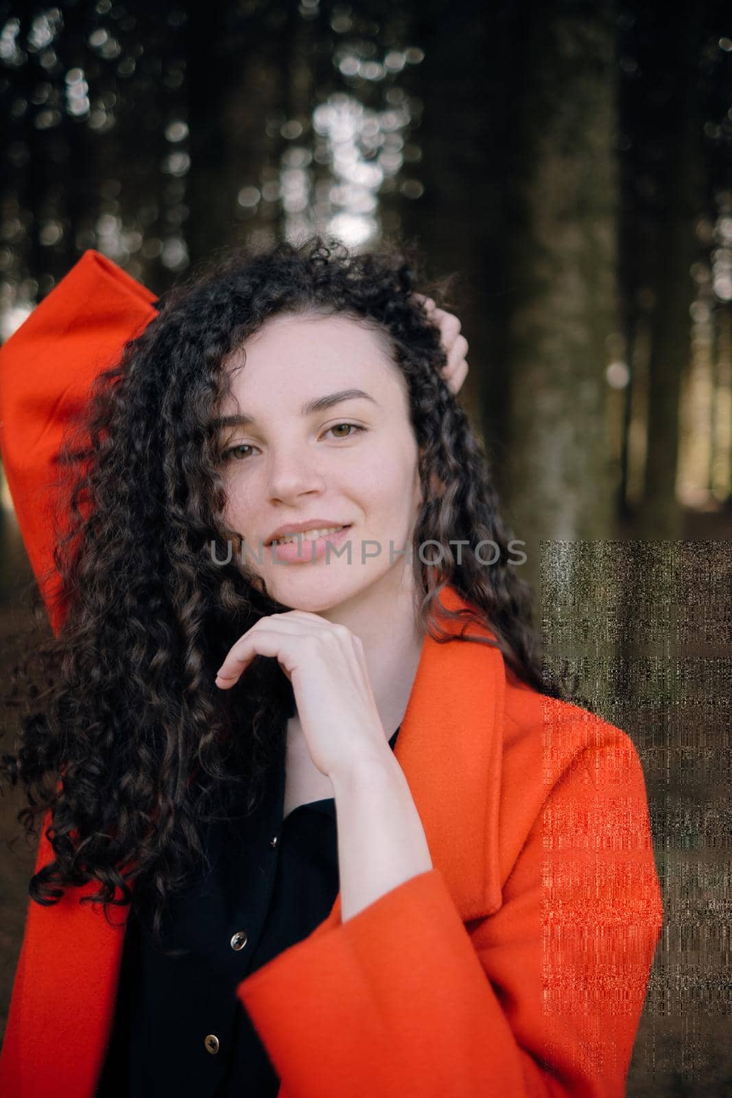 portrait of curly brunette woman in red coat in the park by Symonenko