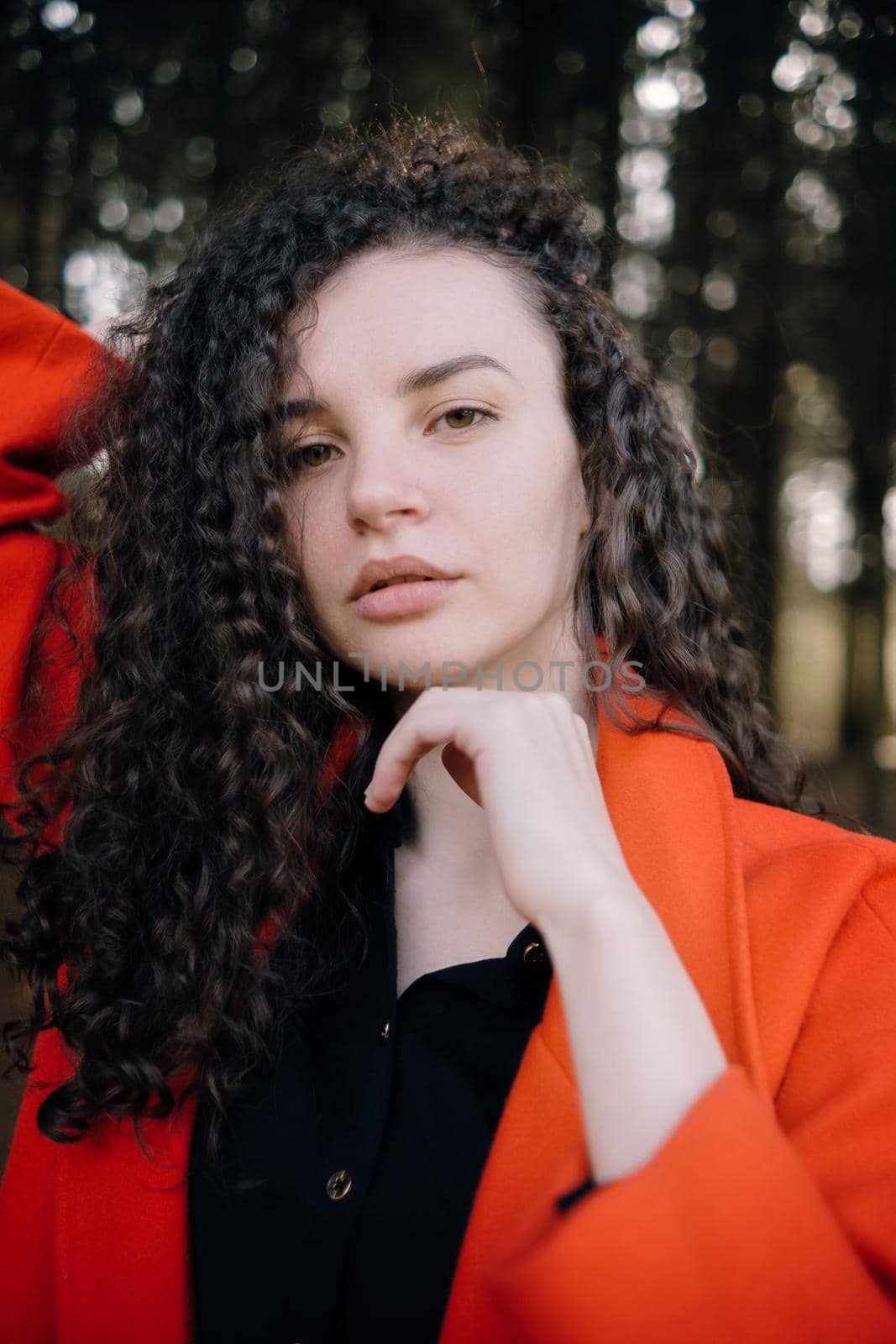 portrait of curly brunette woman in red coat in the park by Symonenko