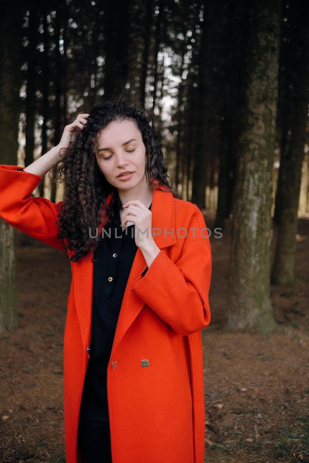 portrait of curly brunette woman in red coat in the park by Symonenko