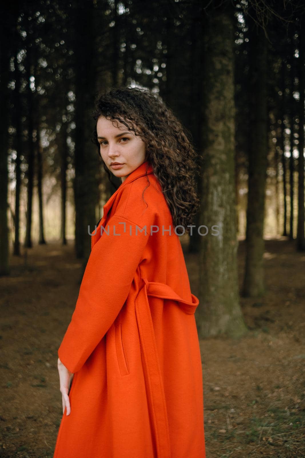 portrait of curly brunette woman in red coat in the park