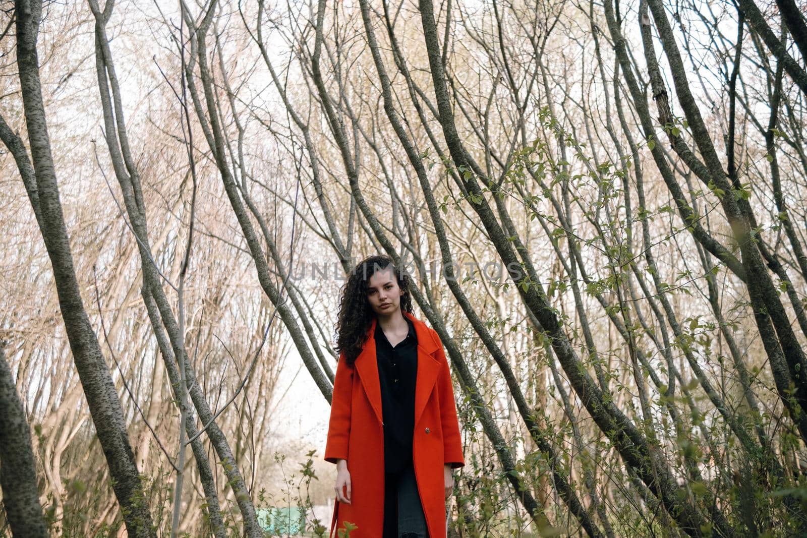 portrait of curly brunette woman in red coat in the park by Symonenko