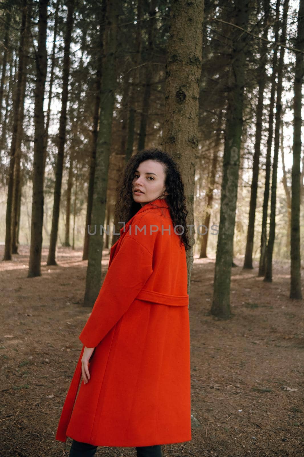 portrait of curly brunette woman in red coat in the park by Symonenko