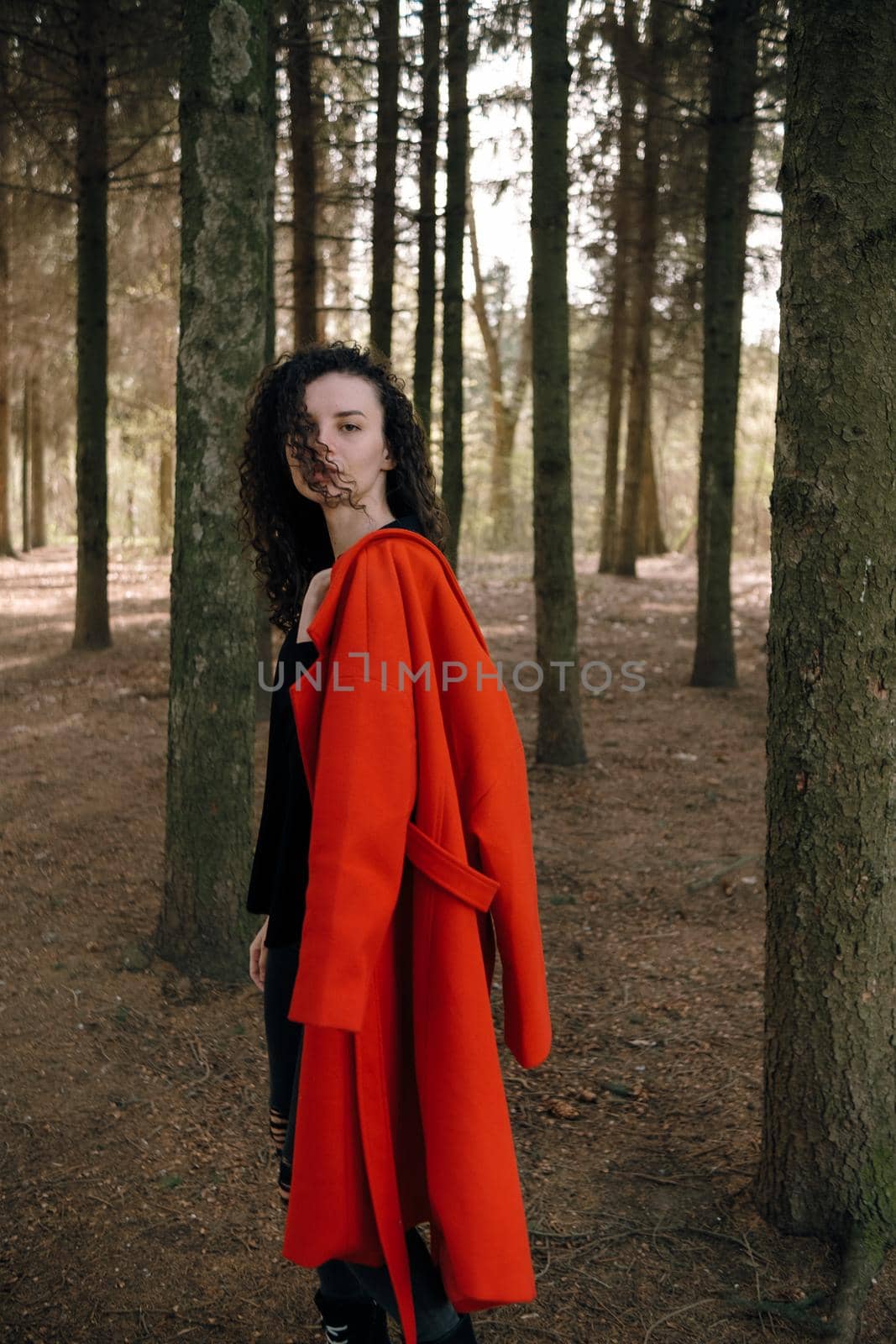 portrait of curly brunette woman in red coat in the park by Symonenko