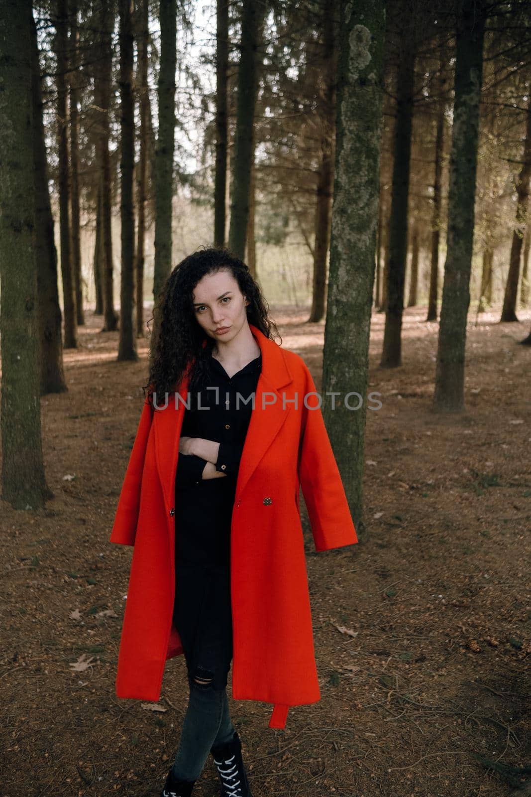 portrait of curly brunette woman in red coat in the park by Symonenko