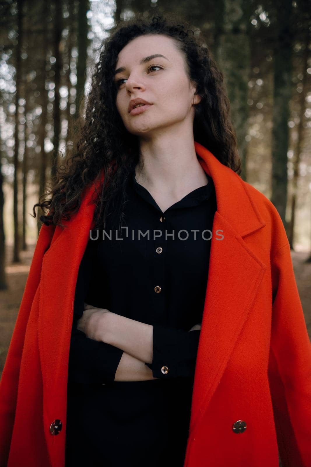 portrait of curly brunette woman in red coat in the park by Symonenko