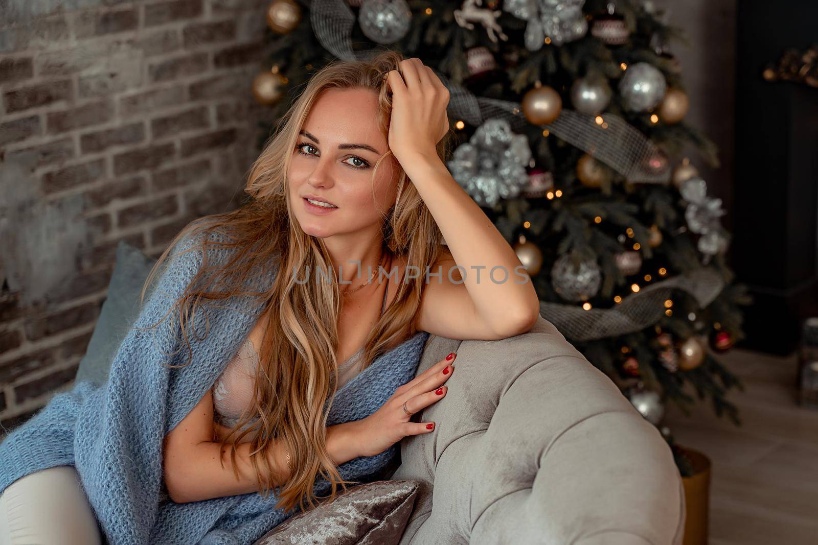 A young blonde woman is sitting on the sofa. The room is decorated with a Christmas tree. by Matiunina
