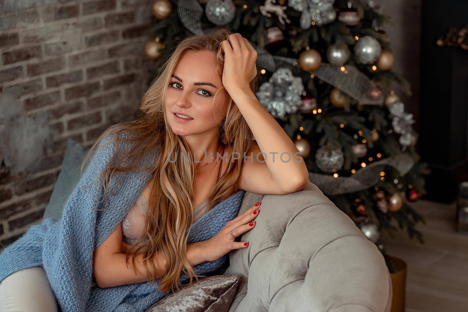 A young blonde woman is sitting on the sofa. The room is decorated with a Christmas tree