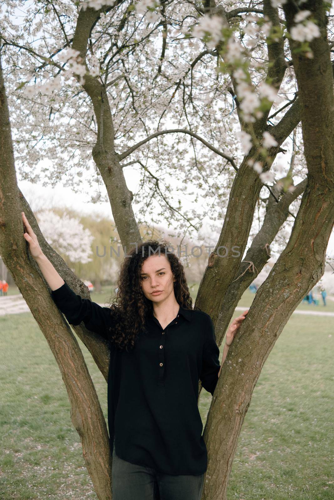 portrait of curly brunette woman in red coat in the park by Symonenko