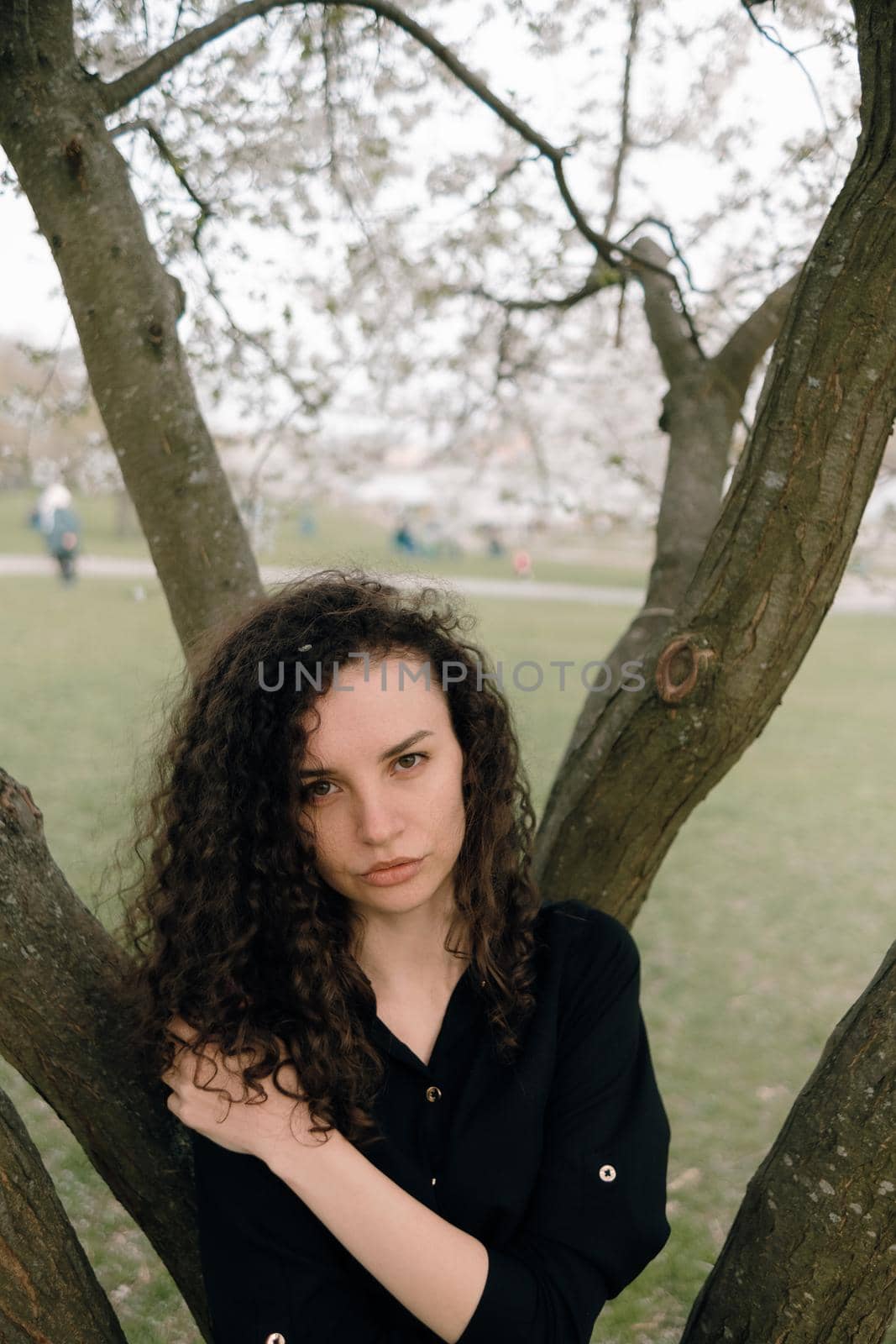 portrait of curly brunette woman in red coat in the park by Symonenko