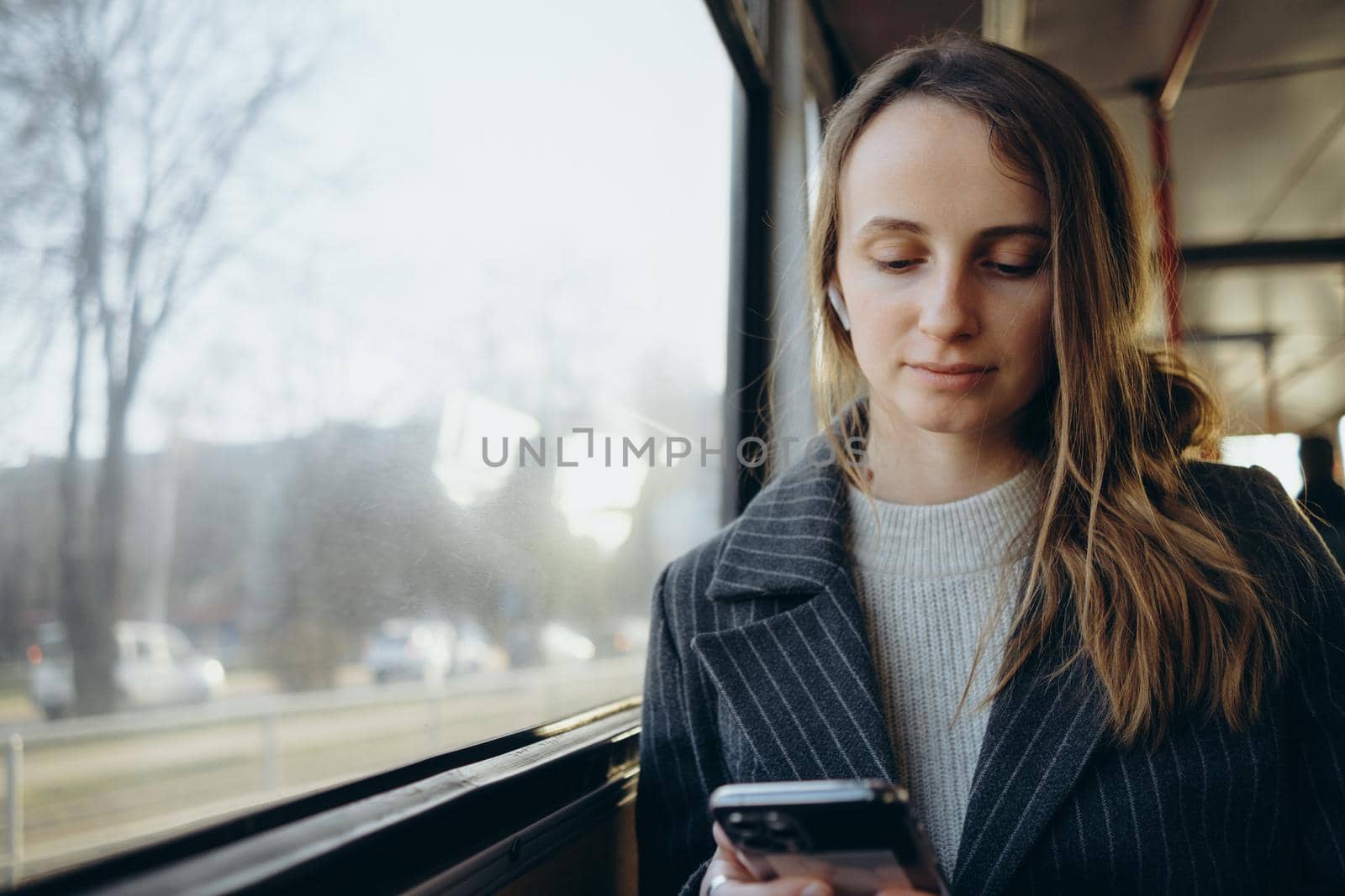 Young woman sadly looking out bus window, wear earphones by Symonenko