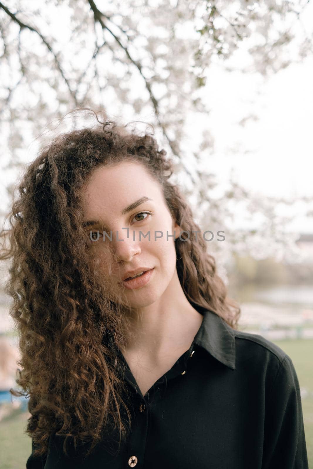 portrait of curly brunette woman in red coat in the park by Symonenko