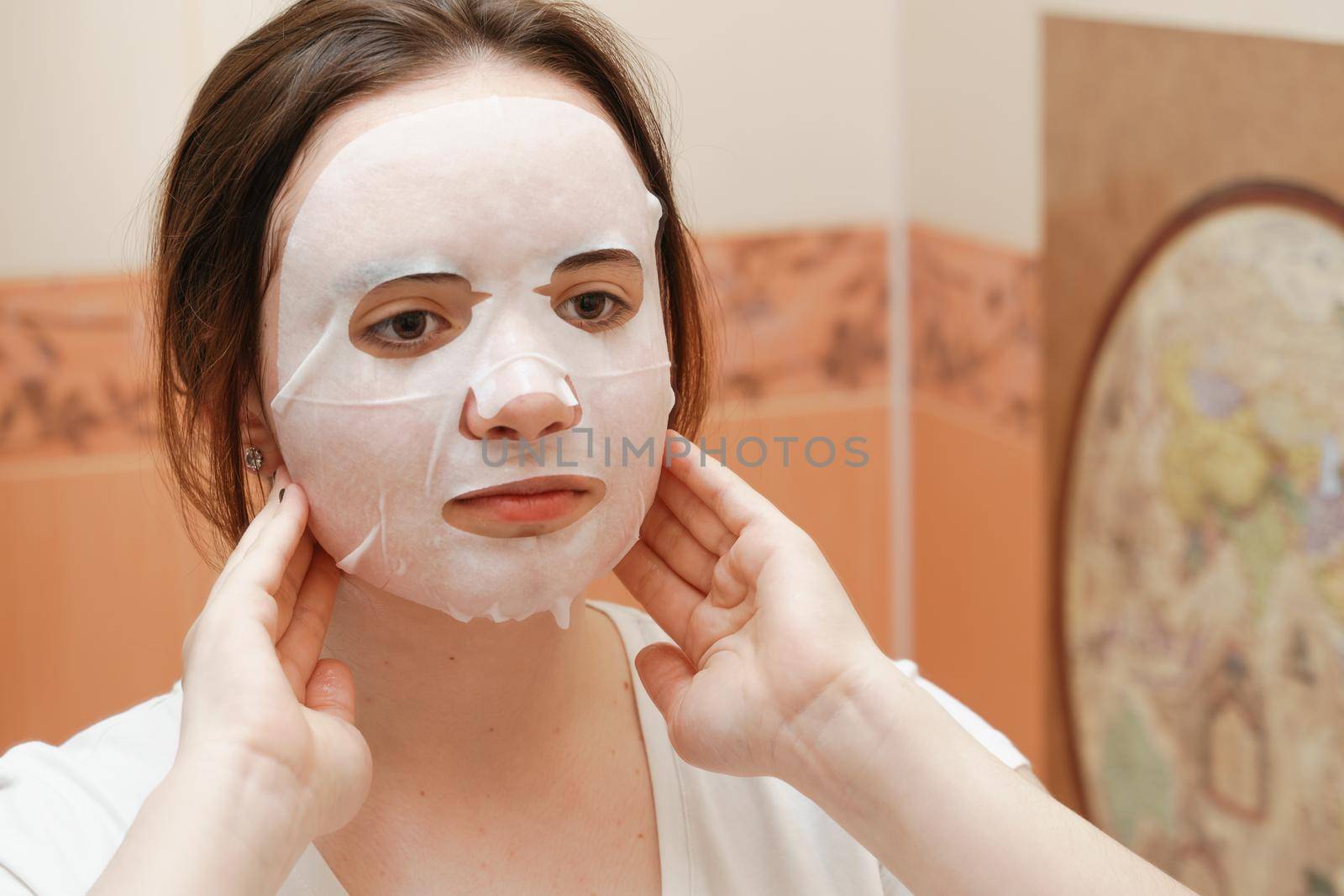 A cheerful and funny girl fooling around and grimacing in a moisturizing face mask. Morning beauty treatments, oily and combination skin care concept. by Matiunina