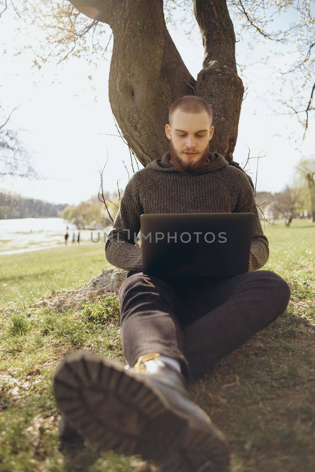 Young man using and typing laptop computer in summer grass. by Symonenko