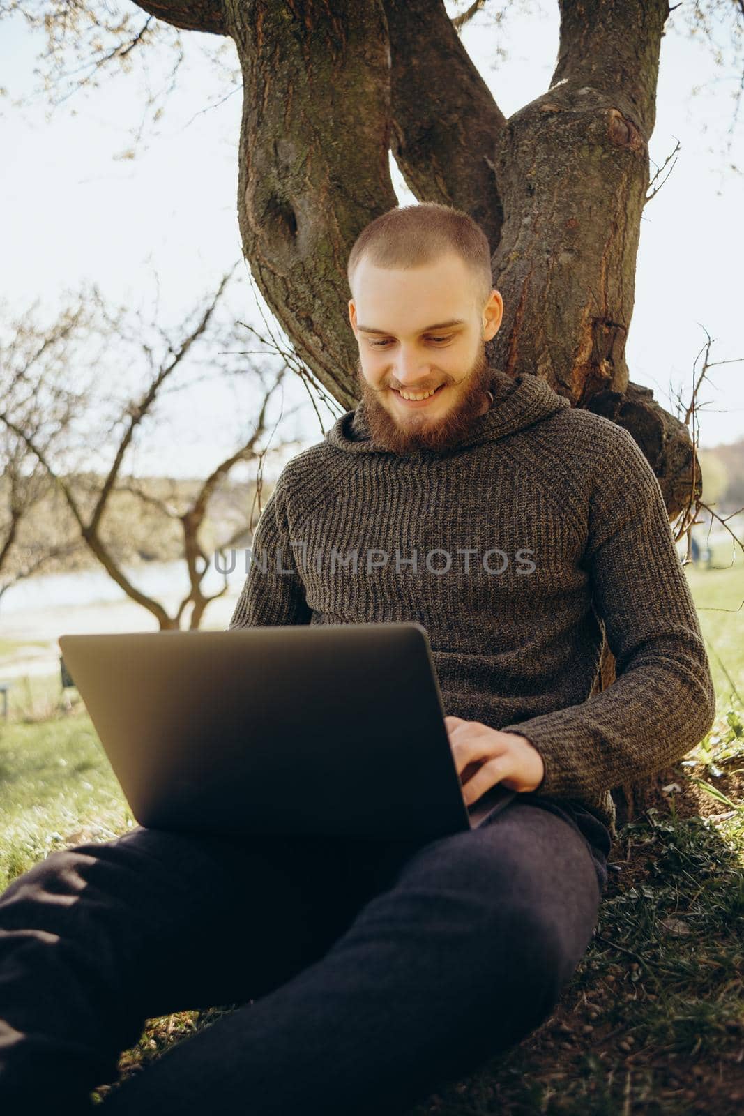 Young man using and typing laptop computer in summer grass.