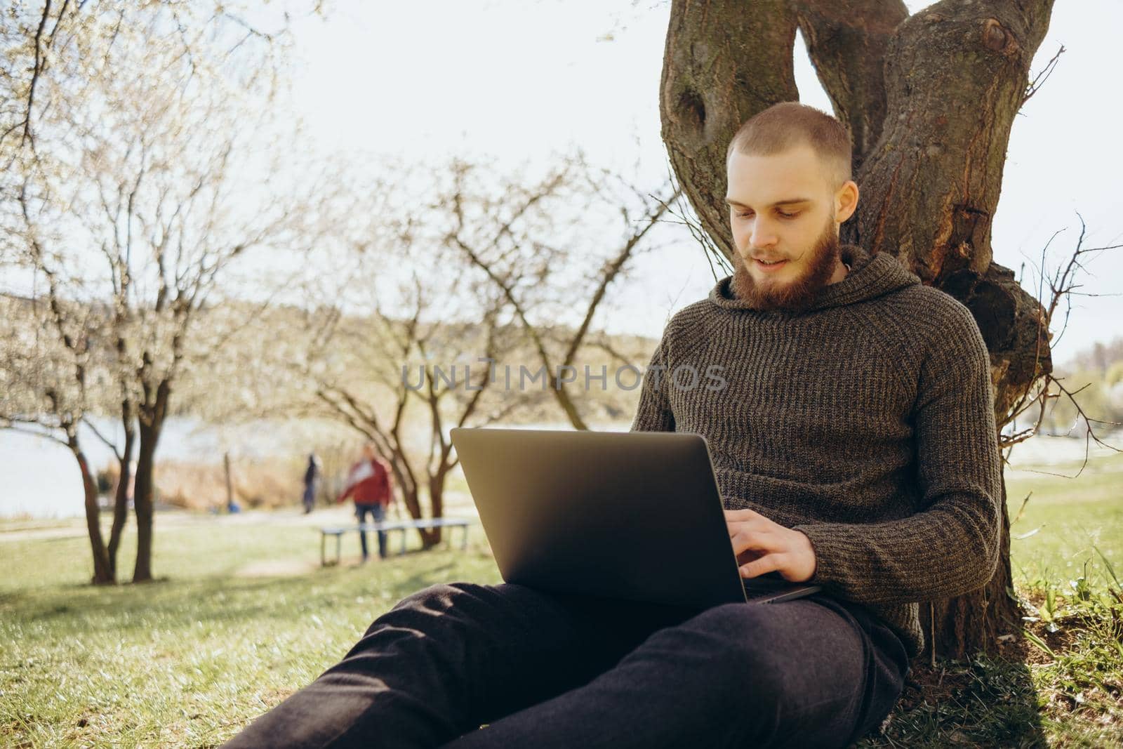 Young man using and typing laptop computer in summer grass.