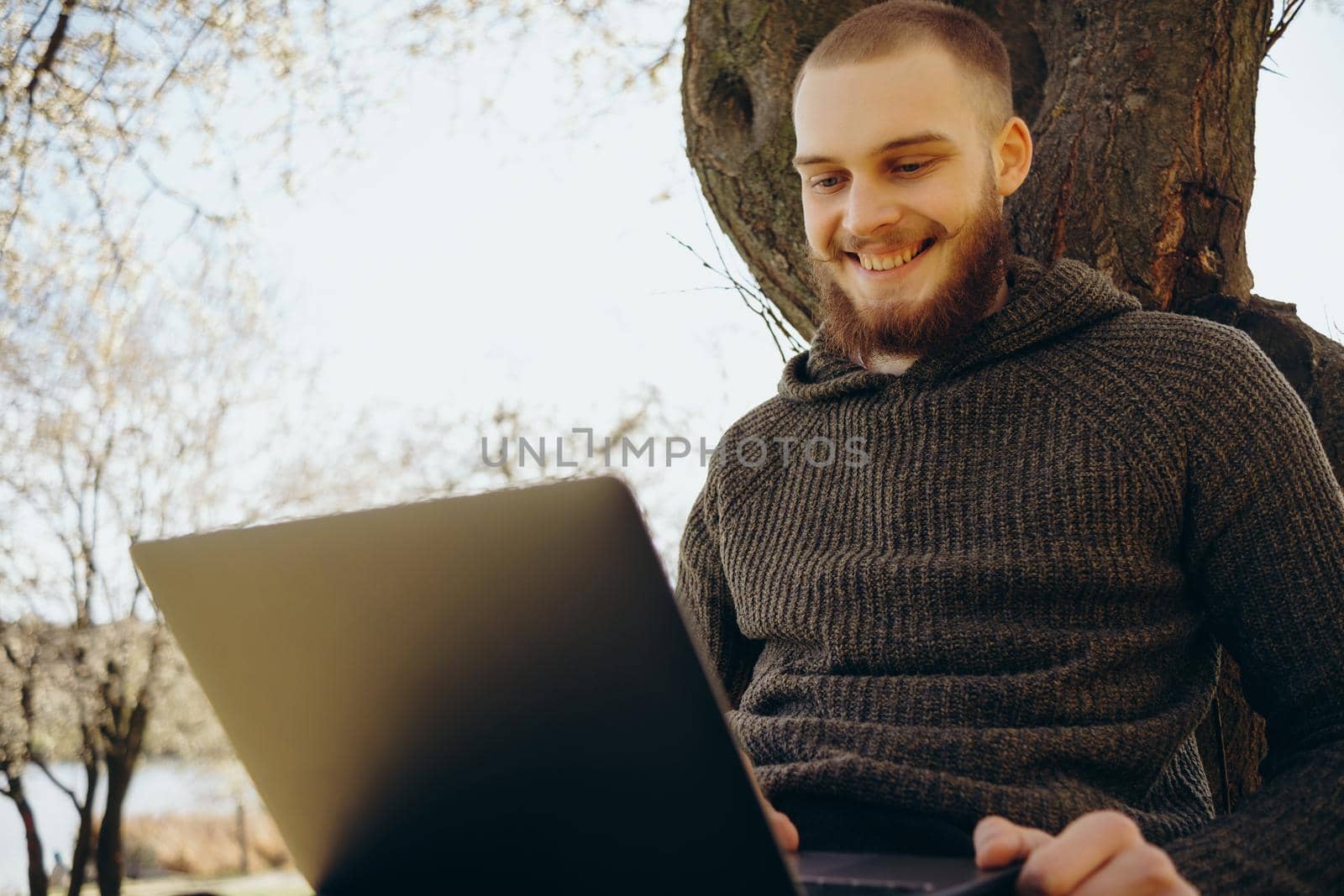Young man using and typing laptop computer in summer grass. by Symonenko
