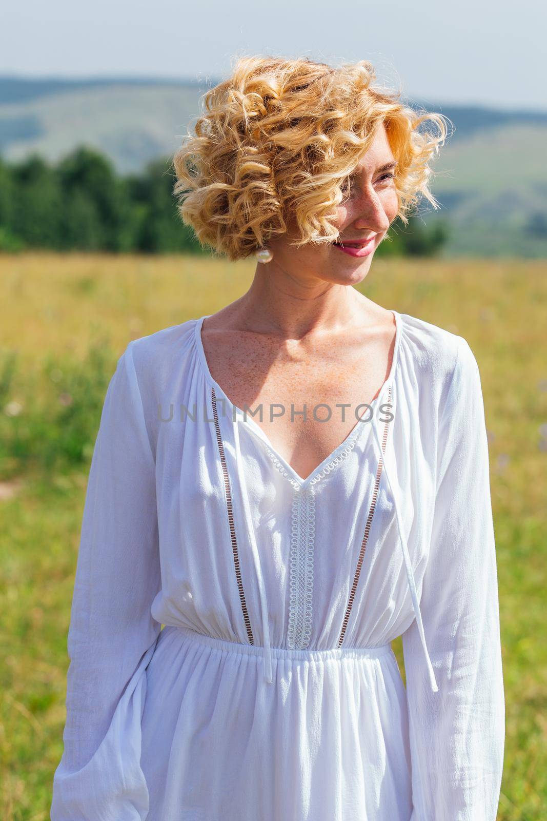 Beautiful blonde woman with short curly hair outdoors. Romantic model in summer white dress.