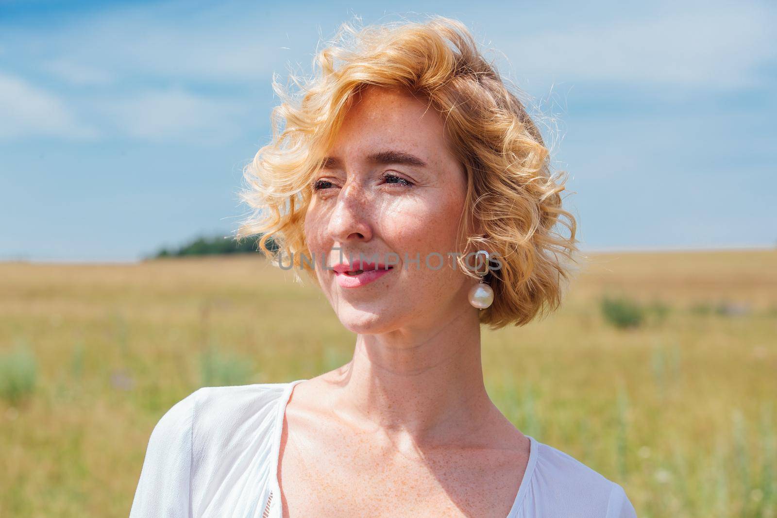 Beautiful blonde woman with short curly hair outdoors. Romantic model in summer white dress.