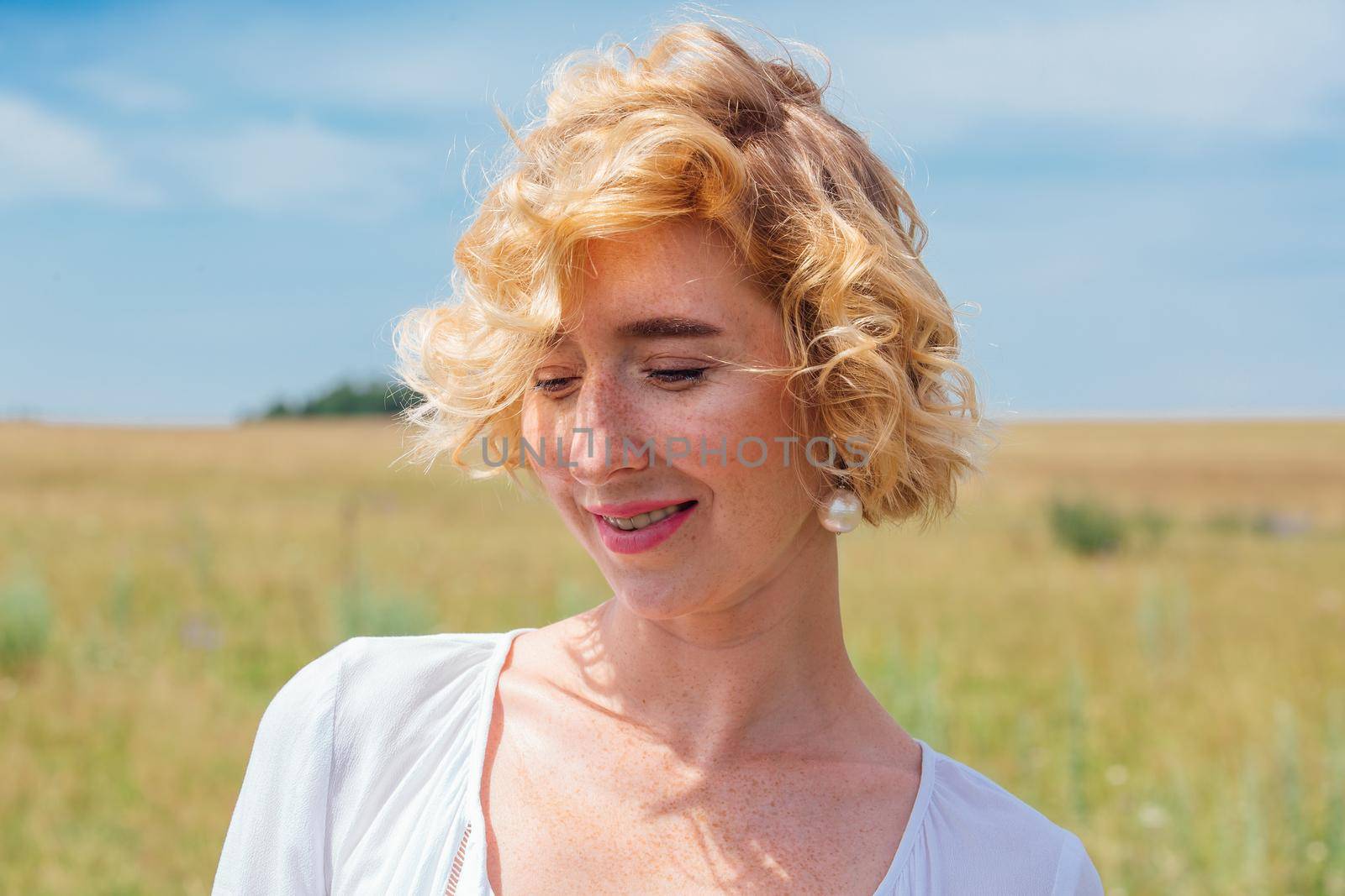 Beautiful blonde woman with short curly hair outdoors. Romantic model in summer white dress.