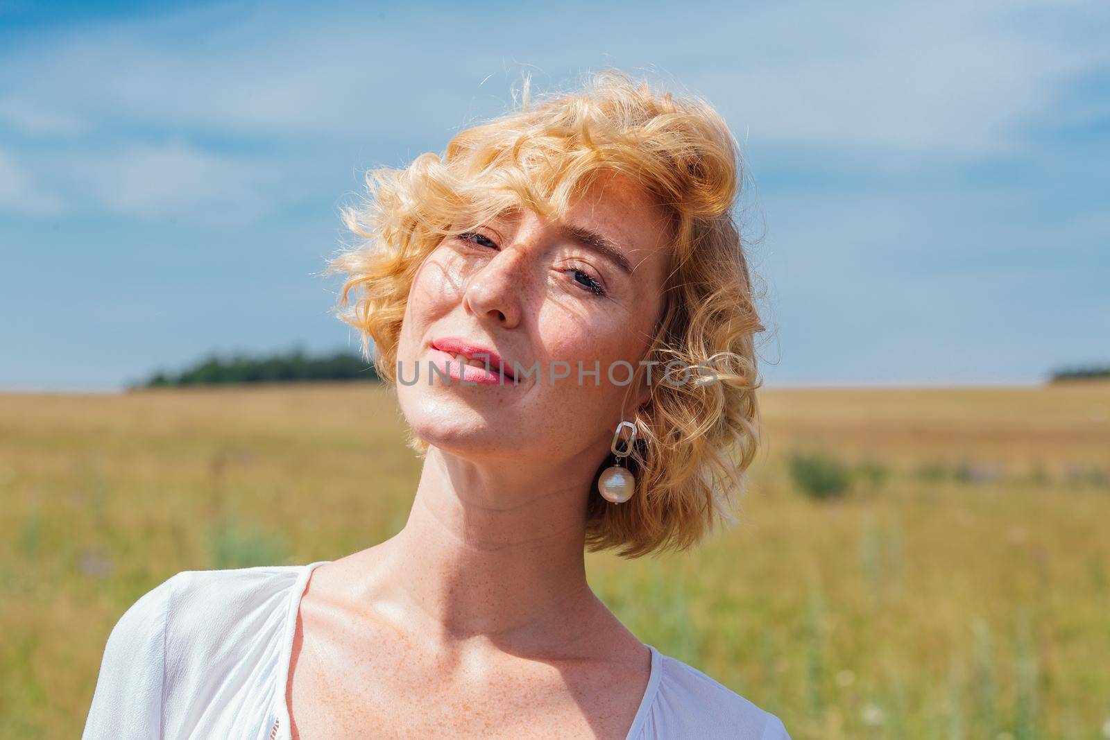 Beautiful blonde woman with short curly hair outdoors. Romantic model in summer white dress.