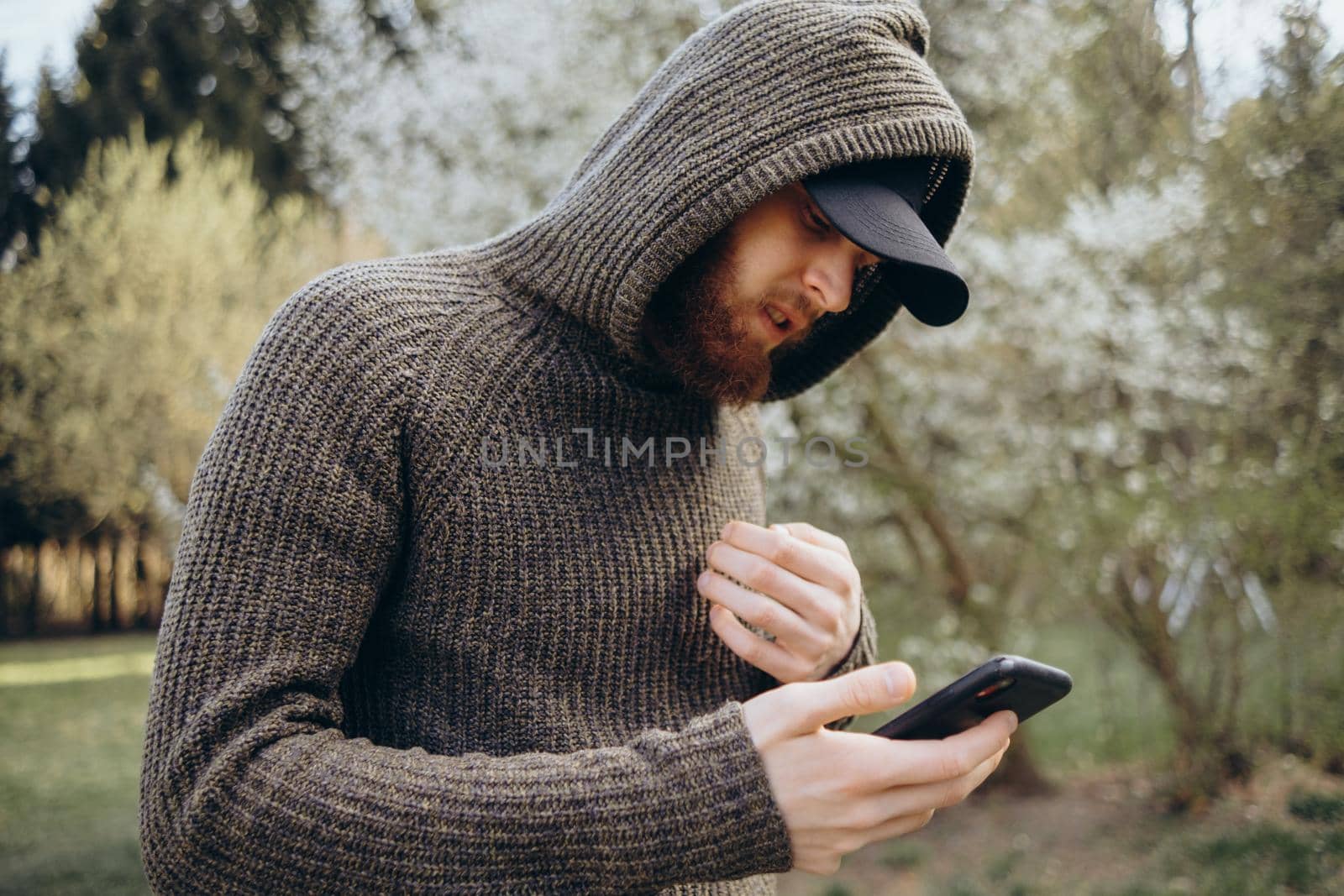 Portrait of young handsome bearded guy in the autumn city park using his phone. Enjoying of the moment of happiness at sunset. by Symonenko