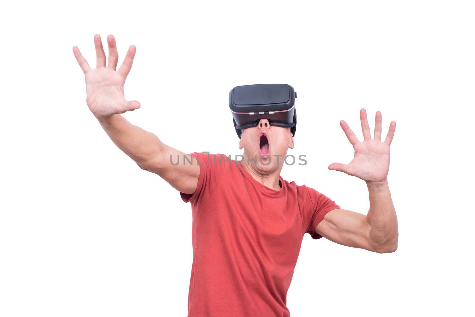 Amazed male gamer in VR goggles exploring virtual reality with outstretched arms and opened mouth while standing isolated on white background