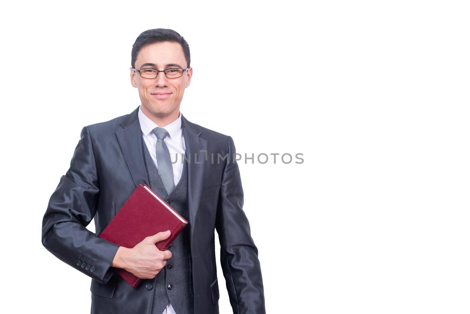 Positive male teacher in formal suit and eyeglasses holding red book and looking at camera with smile isolated on white background