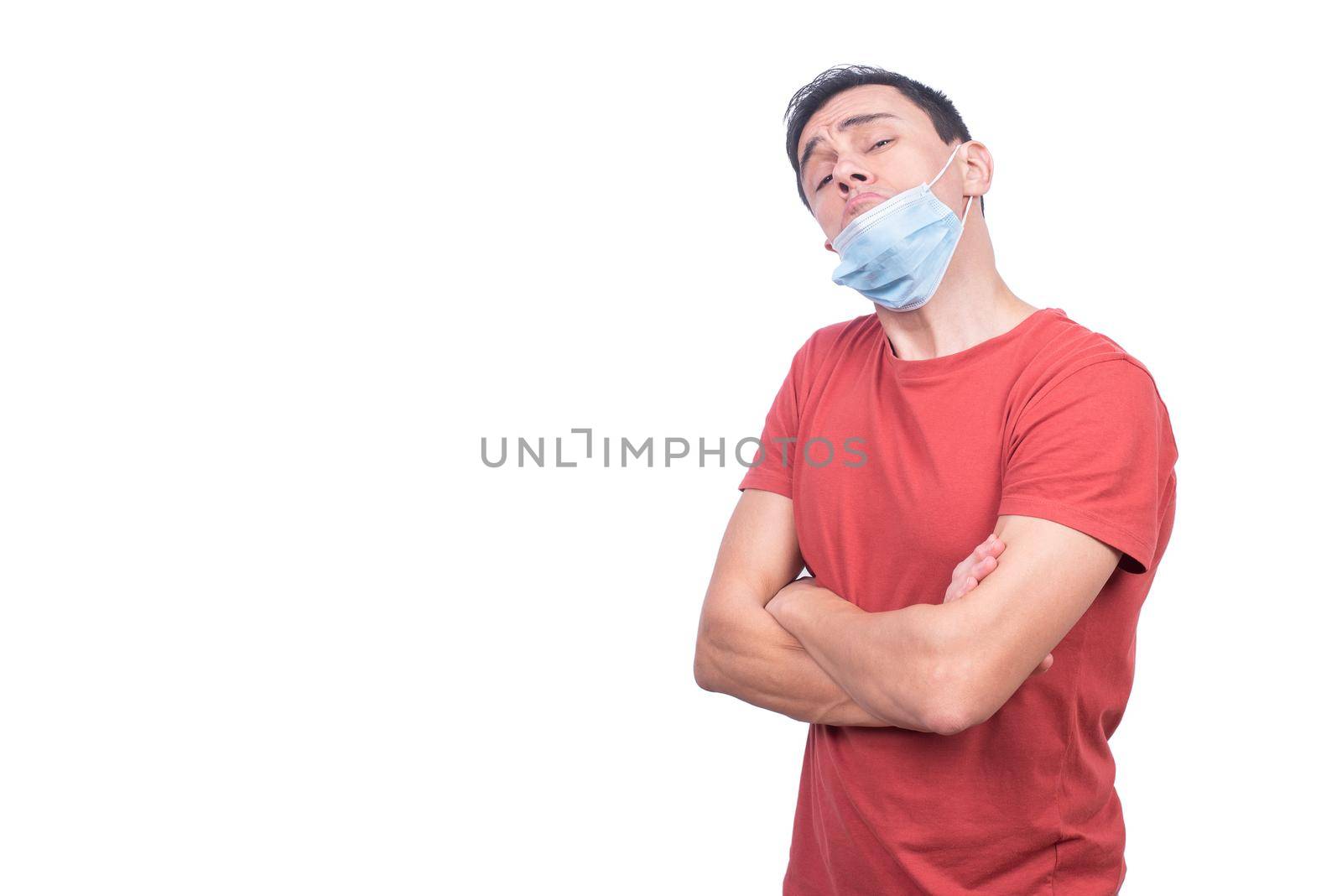 Reckless man with misplaced protective mask looking at camera with crossed arms during coronavirus pandemic isolated on white background in studio