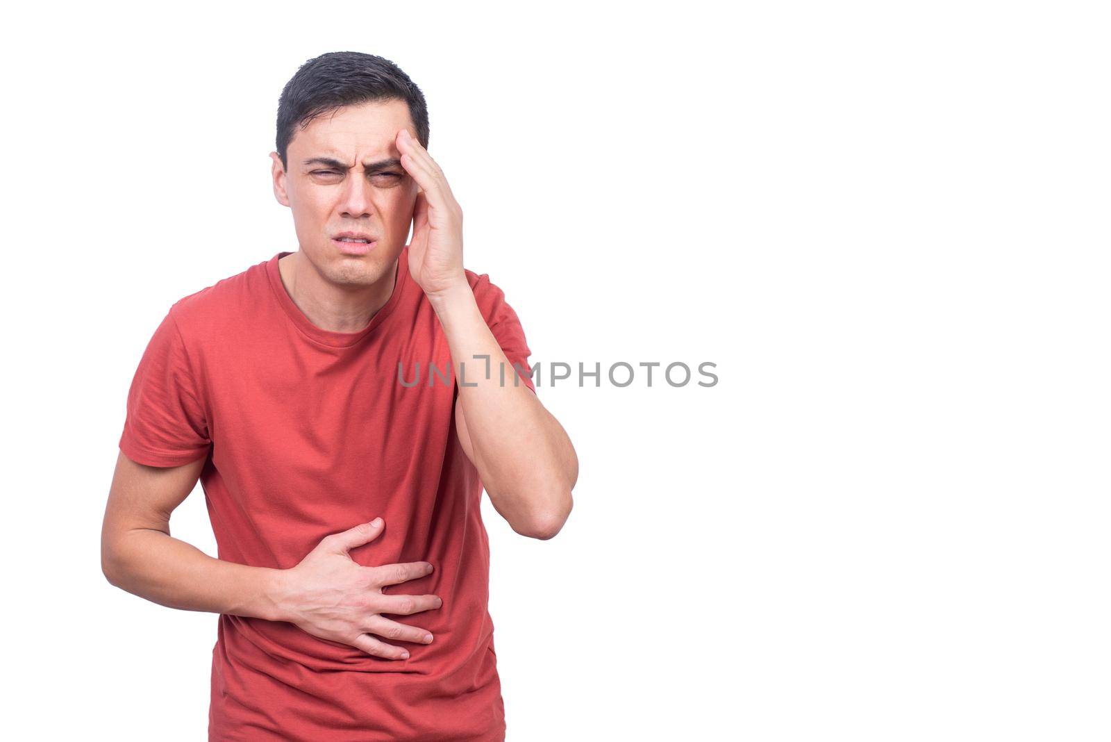 Frowning ill male in casual clothes having headache and holding stomach while standing on white background and looking at camera