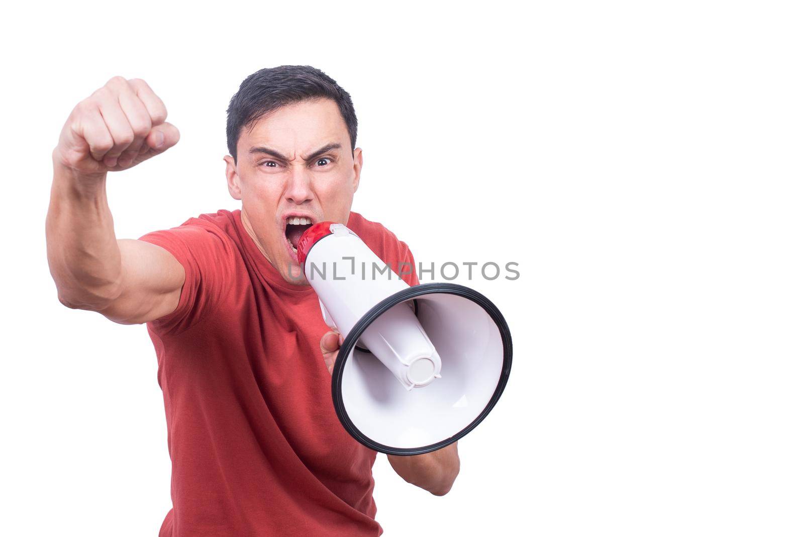 Isolated male model in red t shirt shouting in loudspeaker with raised fist against white background and looking at camera