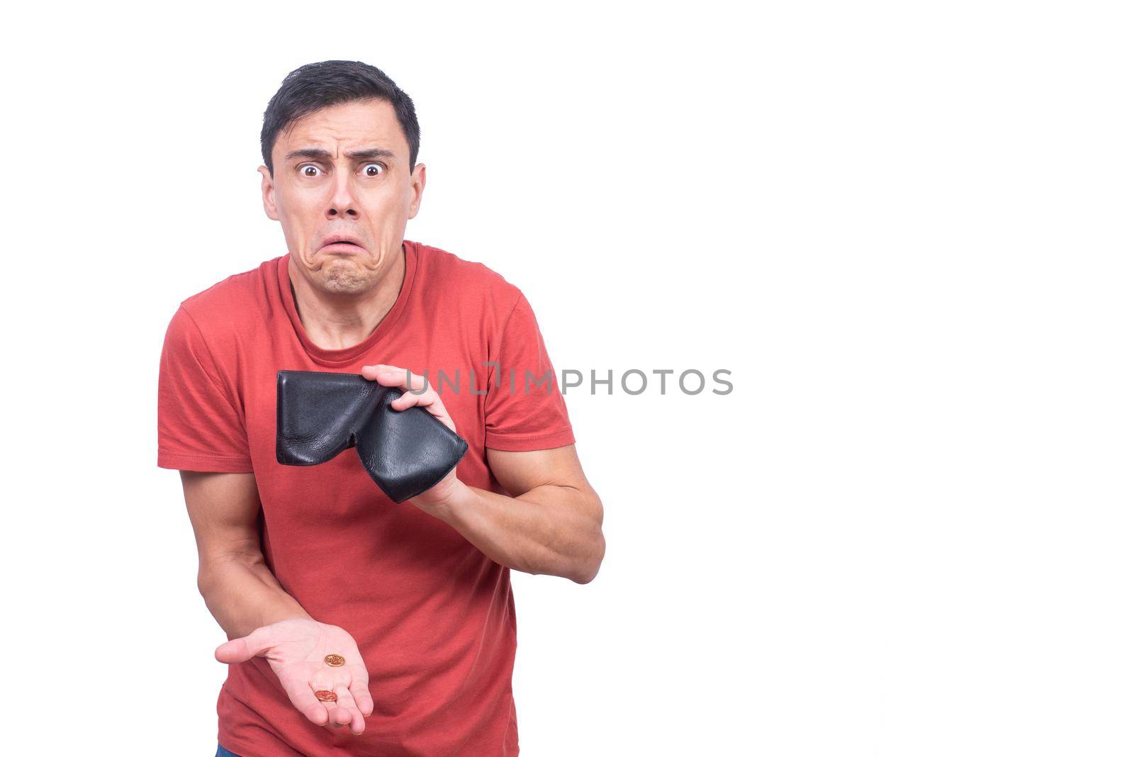 Discouraged male holding few coins and wallet while looking at camera with grimace against blank background in studio