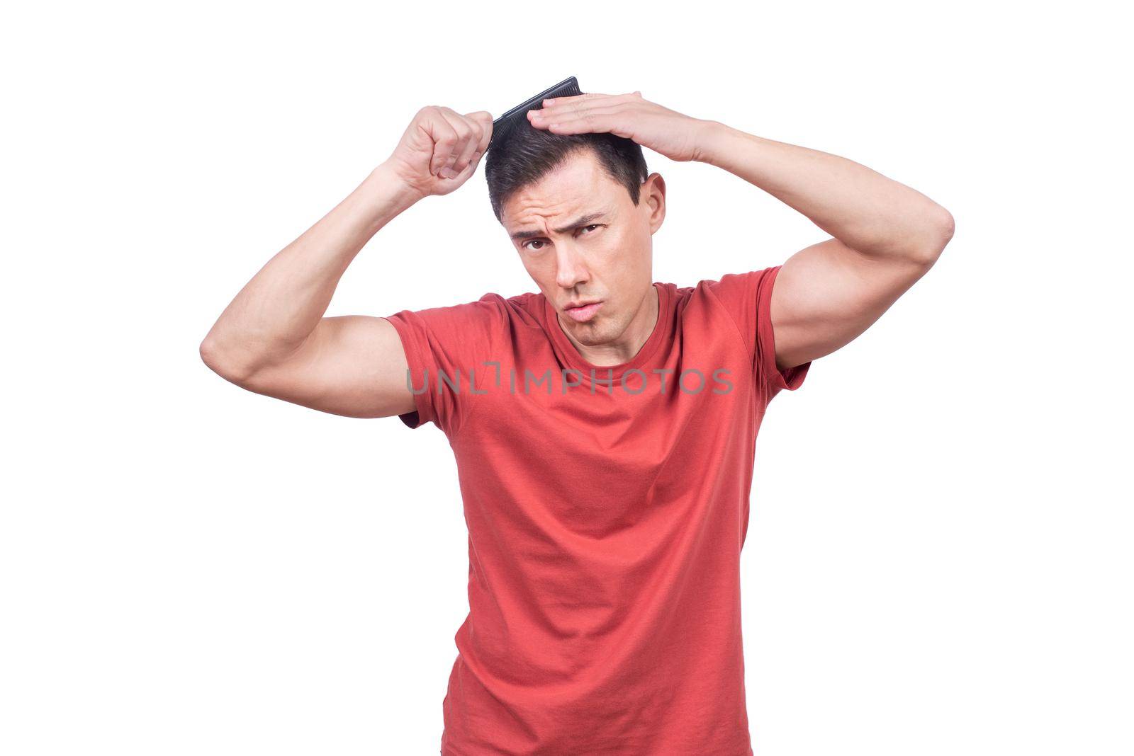 Focused smug male model in casual clothes standing on white background in studio while touching head and brushing dark hair