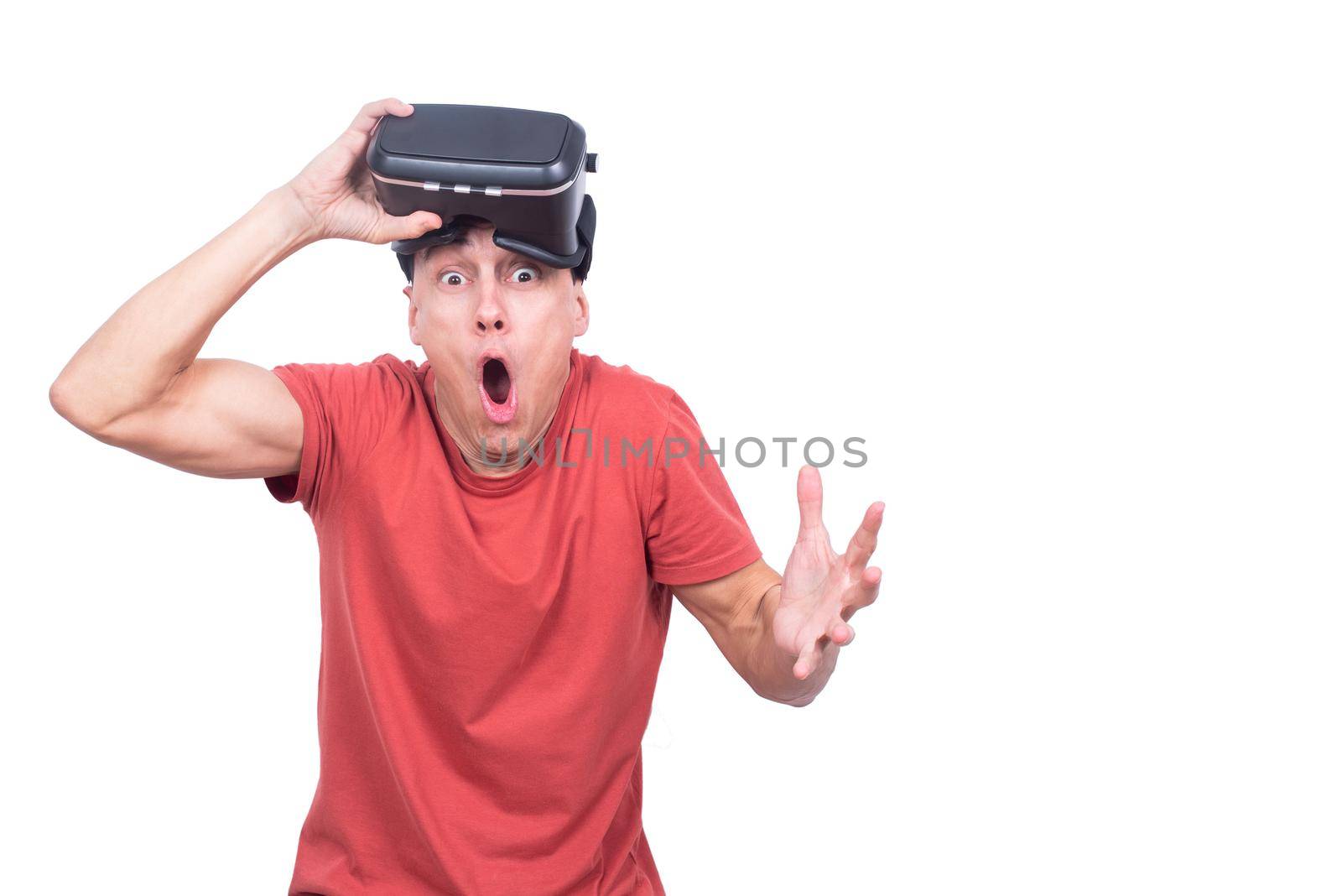 Surprised male gamer with VR headset looking at camera with opened mouth while standing isolated on white background in light studio