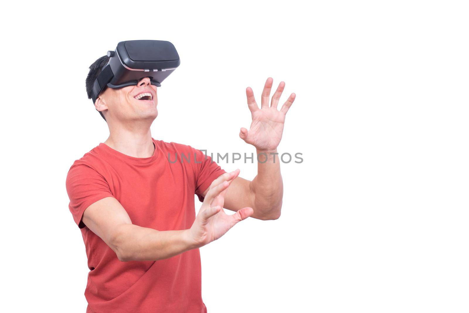 Positive male gamer in modern VR headset exploring virtual reality with smile while standing on white background in light studio