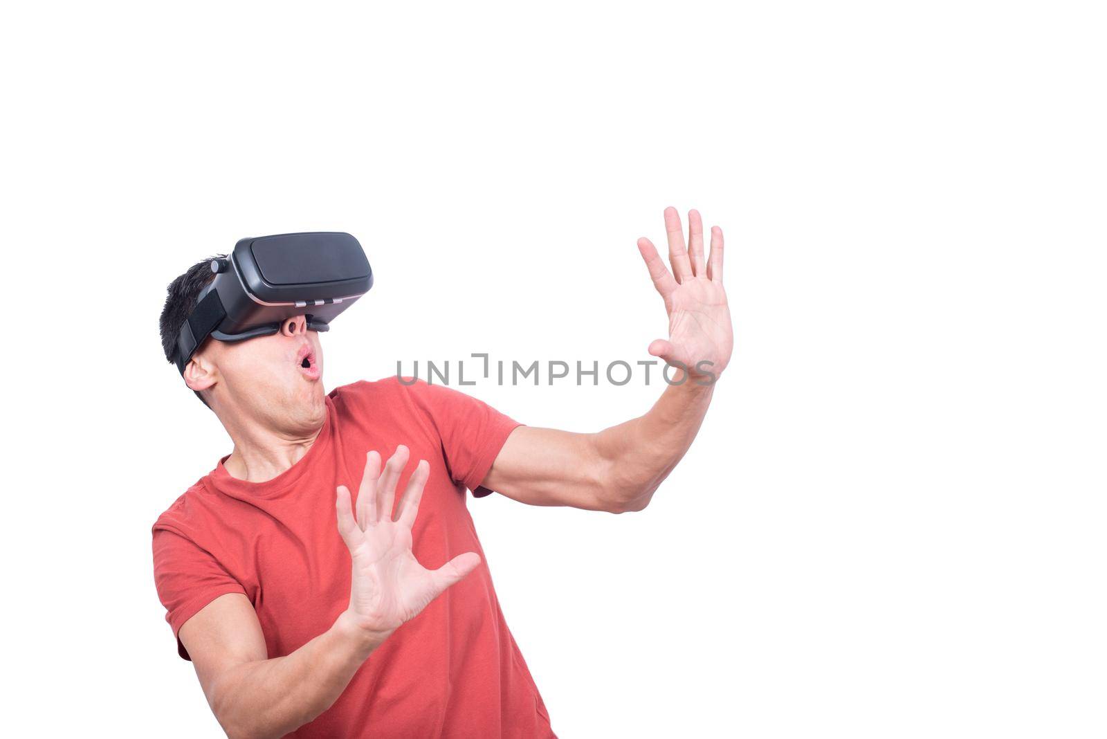 Astonished male gamer with opened mouth in modern VR goggles exploring virtual reality while standing isolated on white background in light studio