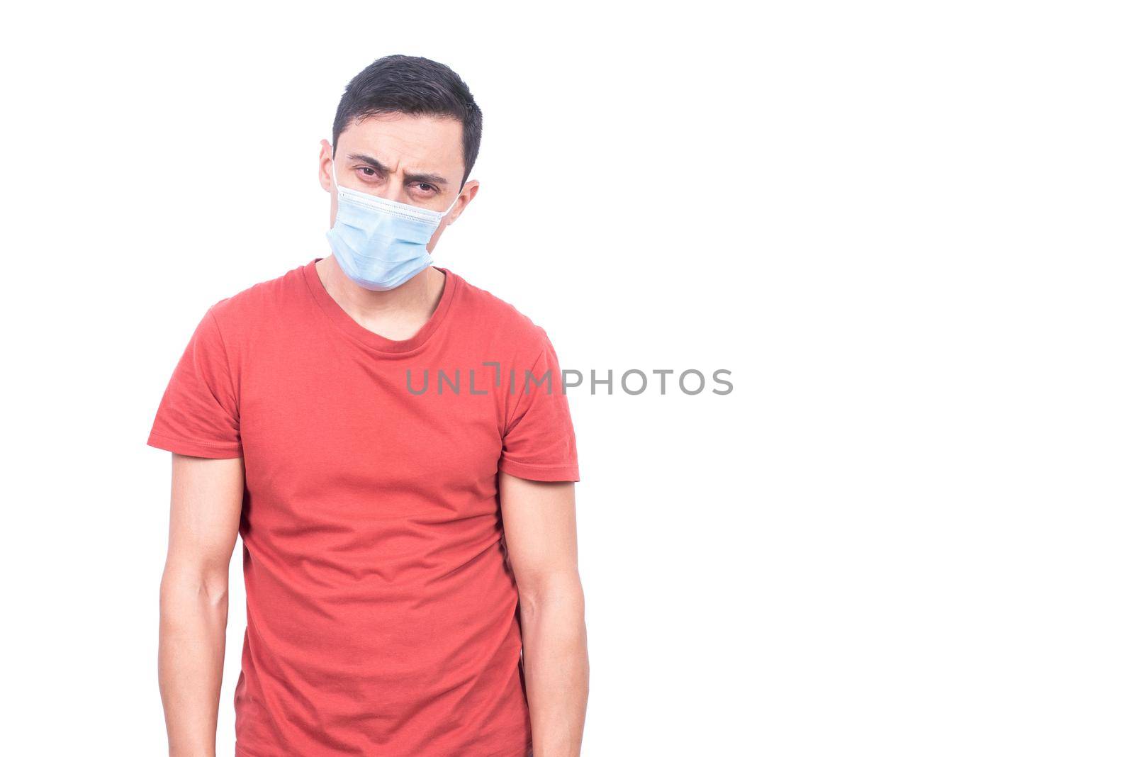 Sad sick COVID infected male in protective mask looking at camera while standing isolated on white background during coronavirus pandemic