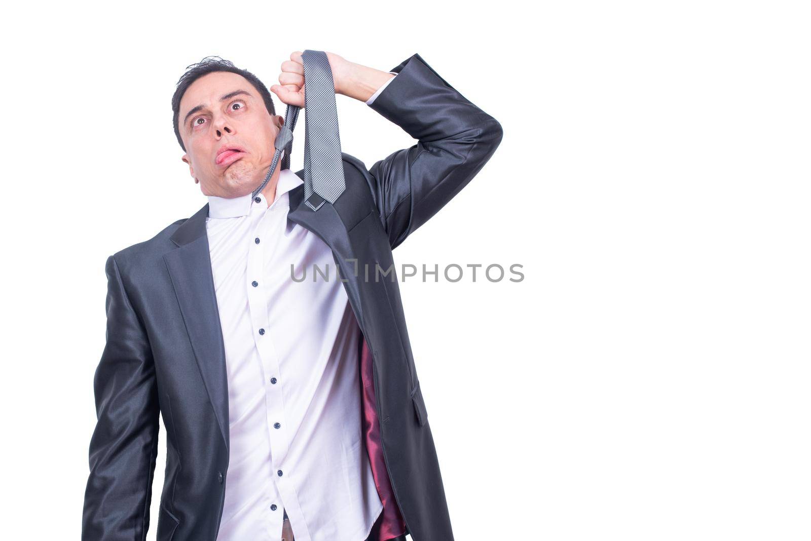 Exhausted male manager in suit with tongue out hanging himself on tie while standing isolated on white background in light studio