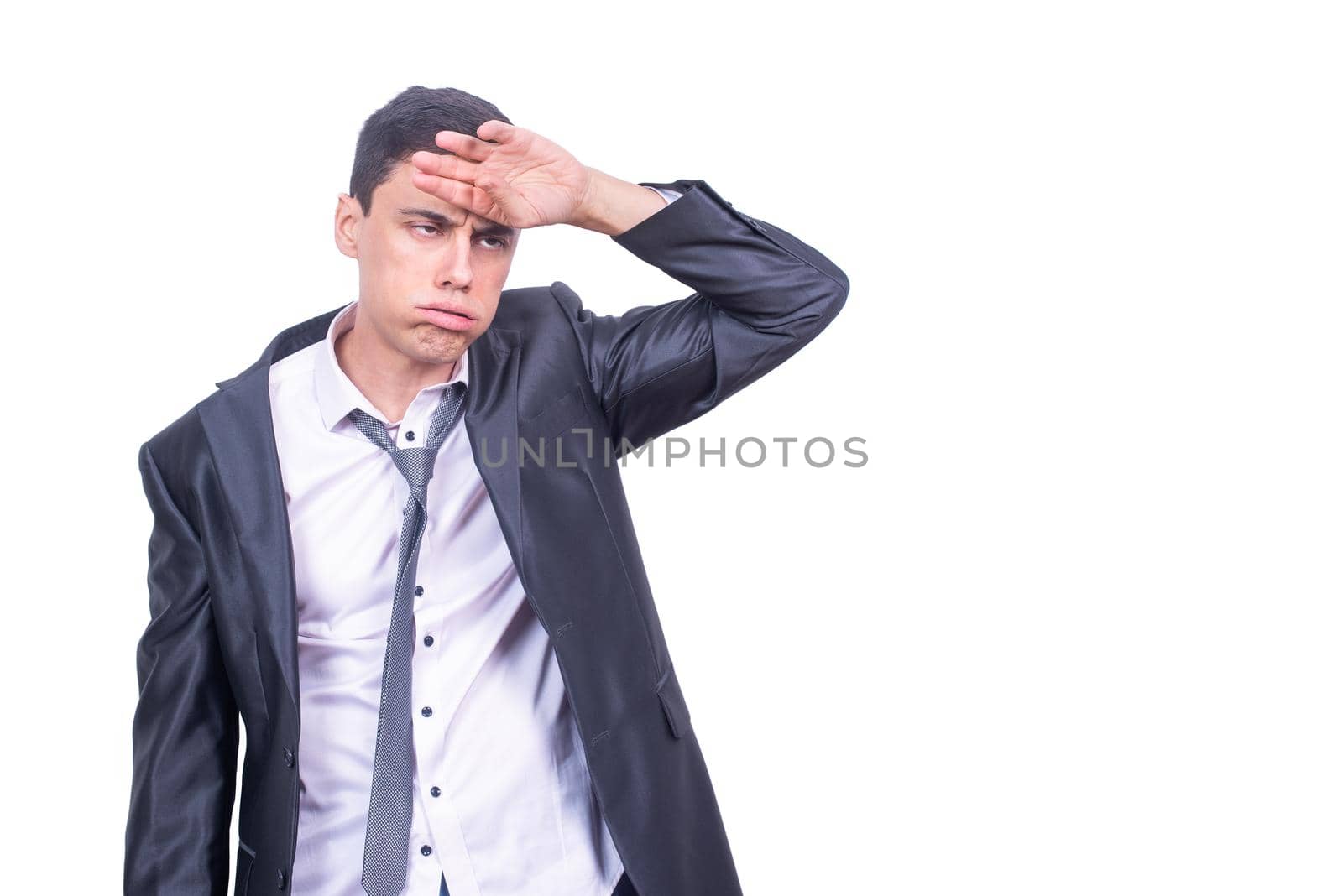 Stressed sloppy male entrepreneur in formal suit touching forehead and exhaling while standing isolated on white background in light studio