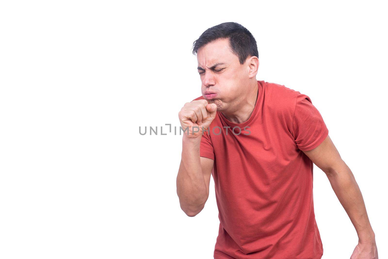 Isolated man in red t shirt coughing with fist near mouth while standing against blank backdrop