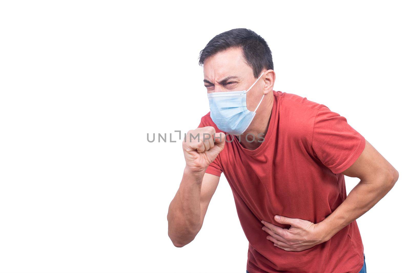 Sick male in t shirt and protective mask coughing standing isolated on white background during coronavirus epidemic in light studio
