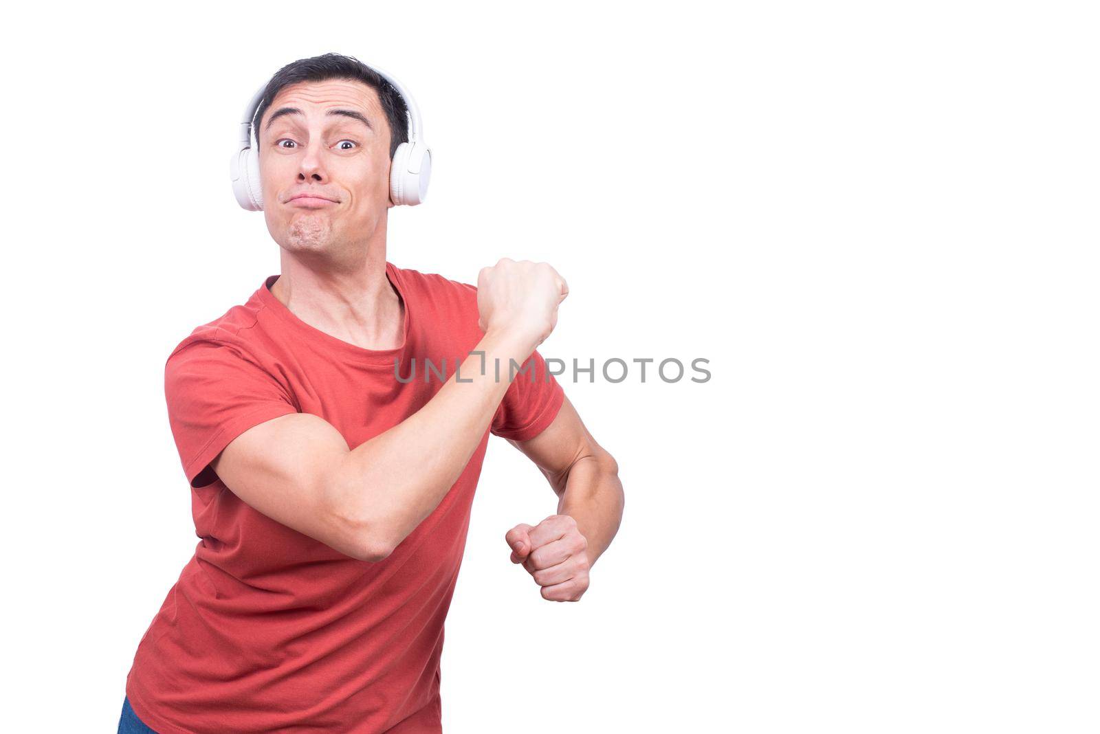 Content male model looking at camera during dance while listening to music in wireless headphones against blank backdrop